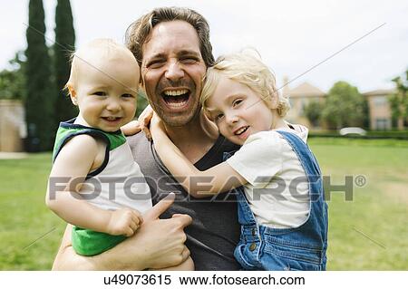 Stock Photography - Portrait of father carrying sons (12-17 months, 4-5) in park. Fotosearch