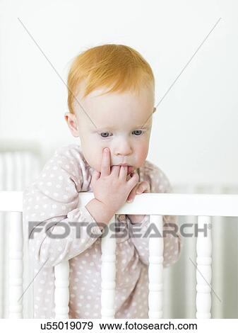 Stock Photo - Portrait of girl ( 12-17 months ) holding fingers in mouth. Fotosearch
