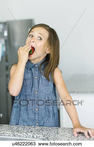 Stock Image - Portrait of girl (6-7) eating strawberry. Fotosearch