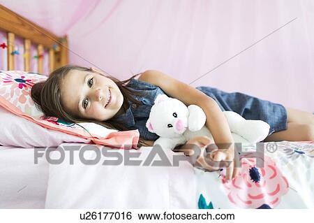 Stock Photograph - Portrait of girl (6-7) lying on bed. Fotosearch