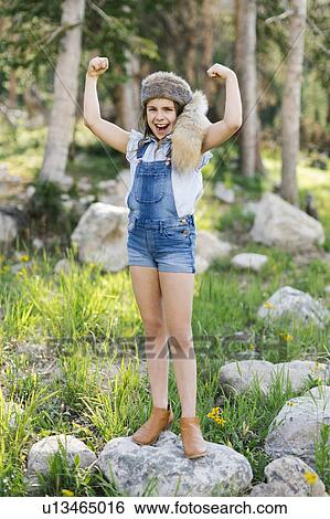 Stock Photograph - Portrait of girl (8-9) flexing muscles in forest. Fotosearch