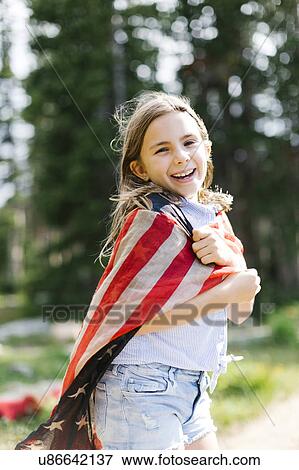 Stock Photo - Portrait of girl (8-9) wrapped in us flag in forest. Fotosearch