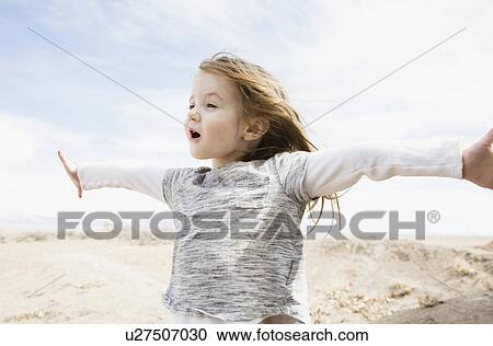 Stock Image - Portrait of little girl (4-5) with outstretched arms and open mouth in field. Fotosearch