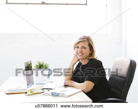Stock Image - Portrait of Mature woman in office with hand on chin. Fotosearch