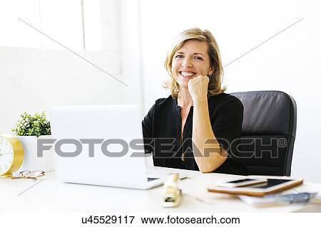 Stock Photo - Portrait of Mature woman in office with hand on chin. Fotosearch