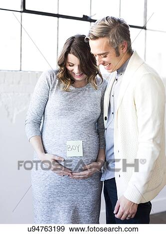 Stock Photo - Portrait of men and smiling pregnant woman with adhesive note on belly. Fotosearch