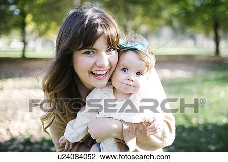 Stock Image - Portrait of mother carrying daughter (12-17 months) in park. Fotosearch