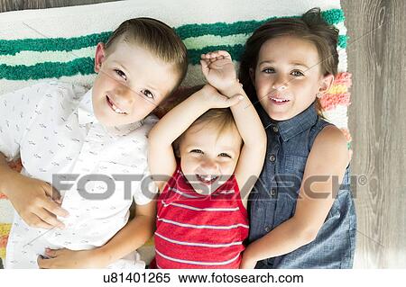 Stock Photography - Portrait of siblings (2-3, 6-7) lying on carpet. Fotosearch