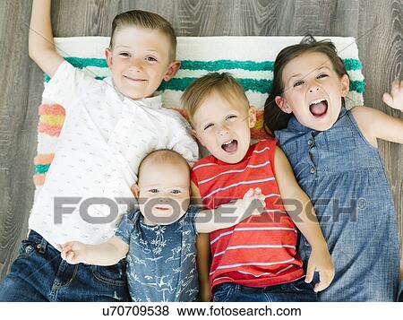 Stock Photo - Portrait of siblings (6-11 months, 2-3, 6-7) lying on carpet. Fotosearch