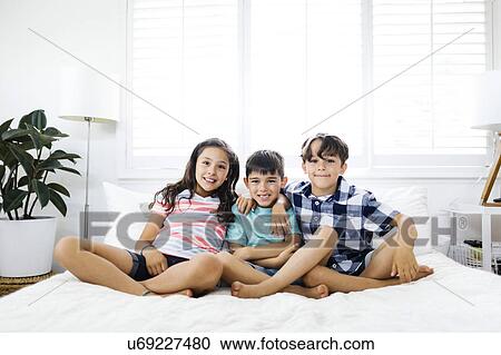 Portrait of smiling brothers ( 6-7, 8-9 ) and sister ( 10-11 ) sitting on bed View Large Photo Image Stock Image - Portrait of smiling brothers ( 6-7, 8-9 ) and sister ( 10-11 ) sitting on bed. Fotosearch