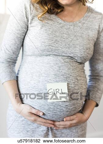 Stock Image - Portrait of smiling pregnant woman with adhesive note on belly. Fotosearch