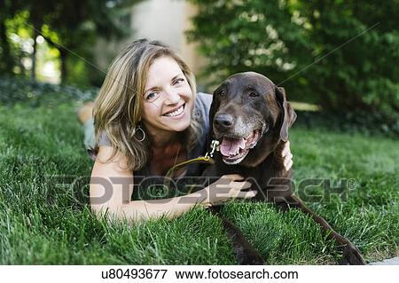 Portrait of smiling woman lying on grass with Labrador Retriever View Large Photo Image Stock Photo - Portrait of smiling woman lying on grass with Labrador Retriever. Fotosearch