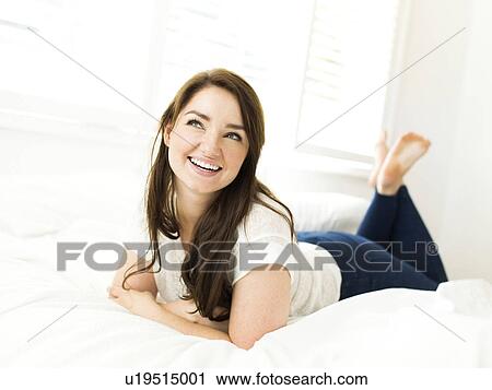 Stock Image - Portrait of woman lying on bed and smiling. Fotosearch