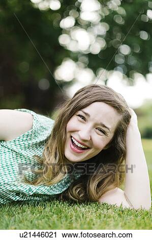 Stock Image - Portrait of woman lying on grass and laughing. Fotosearch