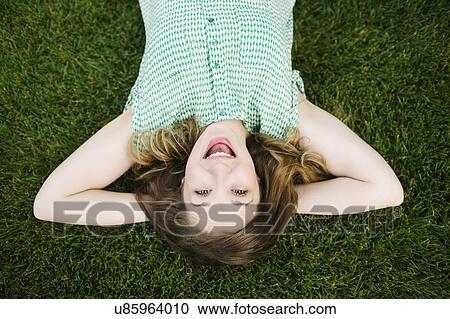 Stock Image - Portrait of woman lying on grass and laughing. Fotosearch