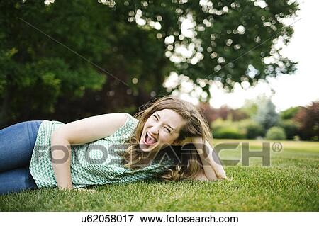 Stock Photo - Portrait of woman lying on grass and laughing. Fotosearch