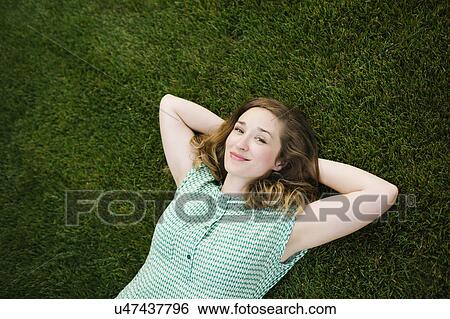 Stock Photograph - Portrait of woman lying on grass and looking at camera. Fotosearch