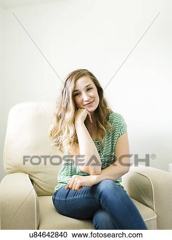 Stock Image - Portrait of woman sitting in living room. Fotosearch