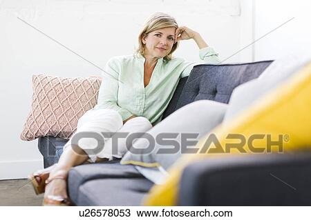 Stock Image - Portrait of woman sitting on sofa. Fotosearch