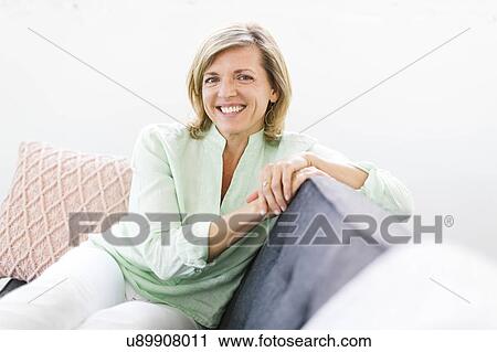 Stock Image - Portrait of woman sitting on sofa. Fotosearch