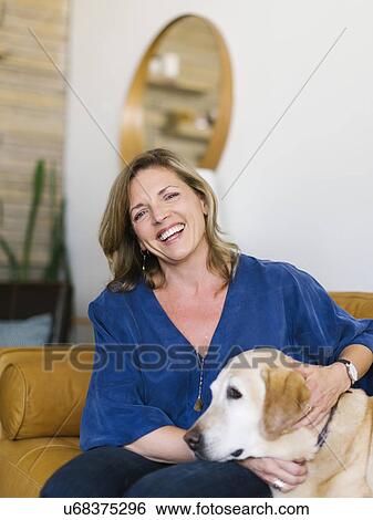 Stock Photograph - Portrait of woman stroking Labrador Retriever on sofa. Fotosearch
