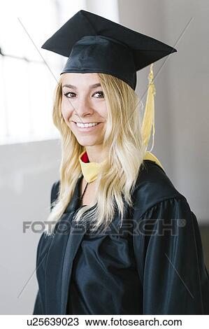 Stock Image - Portrait of young blond woman wearing graduation gown. Fotosearch