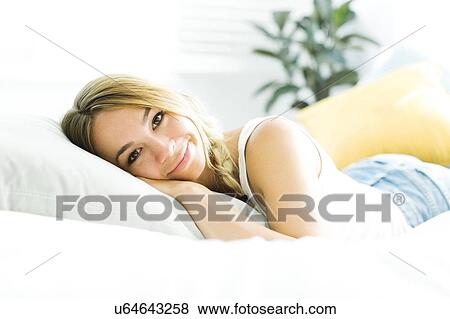 Stock Photo - Portrait of young woman lying on bed. Fotosearch