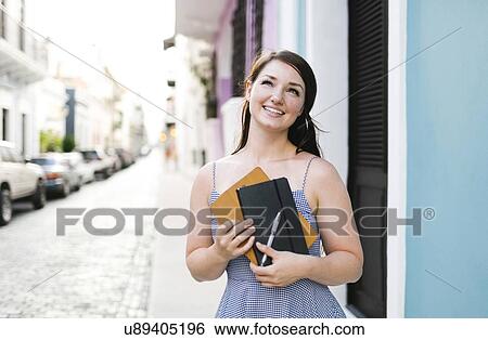 Stock Photograph - Puerto Rico, San Juan, Cheerful woman with digital tablet and notebook walking city streets. Fotosearch