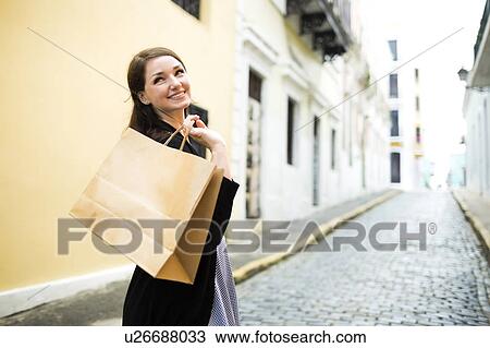 Stock Image - Puerto Rico, San Juan, Woman with shopping bag walking city streets. Fotosearch
