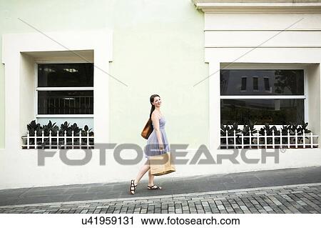 Stock Image - Puerto Rico, San Juan, Woman with shopping bag walking city streets. Fotosearch