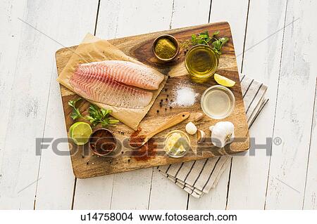Raw tilapia and ingredients on cutting board View Large Photo Image Picture - Raw tilapia and ingredients on cutting board. Fotosearch
