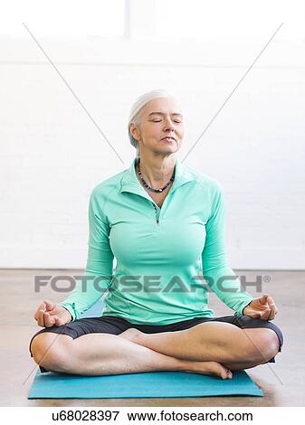 Stock Photo - Senior woman meditating on mat. Fotosearch