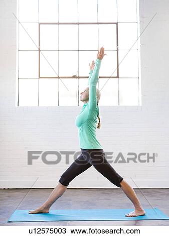 Stock Image - Senior woman practicing yoga on mat. Fotosearch