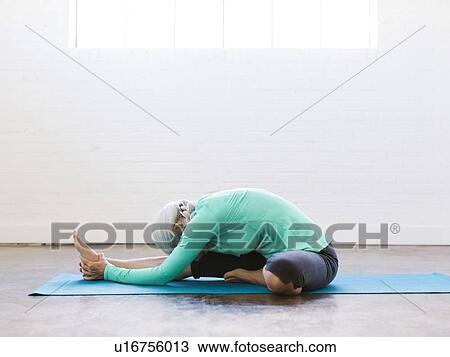 Stock Image - Senior woman practicing yoga on mat. Fotosearch