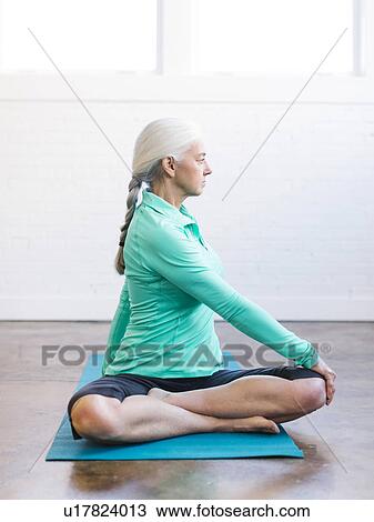 Stock Image - Senior woman practicing yoga on mat. Fotosearch
