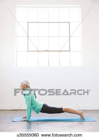 Stock Image - Senior woman practicing yoga on mat. Fotosearch
