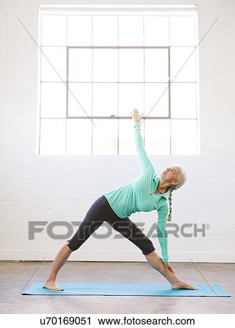 Stock Image - Senior woman practicing yoga on mat. Fotosearch