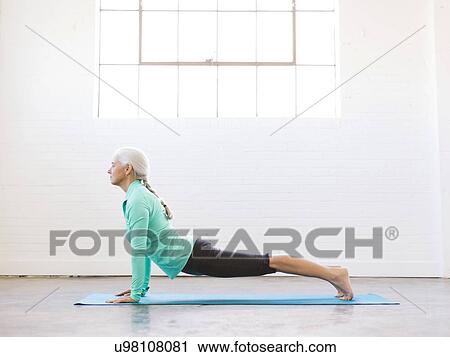 Stock Image - Senior woman practicing yoga on mat. Fotosearch