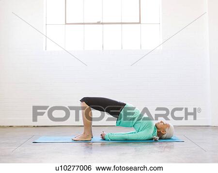 Stock Photograph - Senior woman practicing yoga on mat. Fotosearch