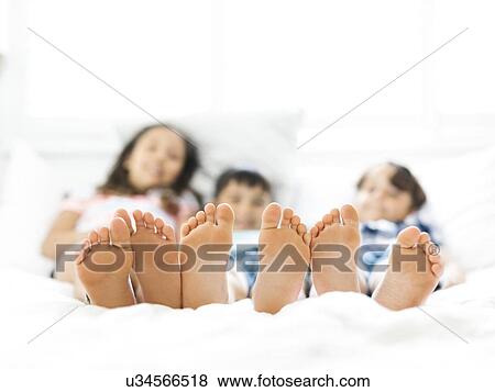 Stock Photo - Siblings (10-11, 6-7, 8-9) lying in bed side by side. Fotosearch