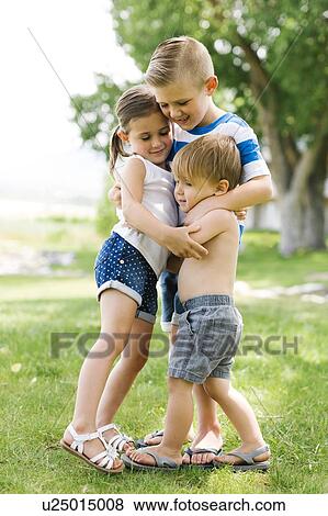 Stock Photo - Siblings (2-3, 4-5, 6-7) embracing in park. Fotosearch