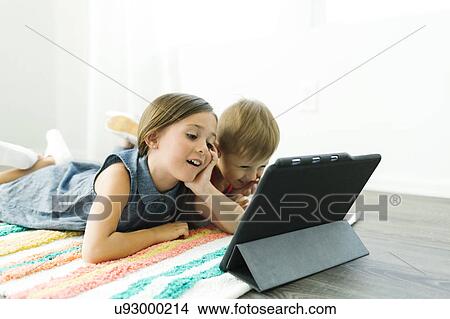 Siblings (2-3, 6-7) lying down on carpet and watching digital tablet View Large Photo Image Picture - Siblings (2-3, 6-7) lying down on carpet and watching digital tablet. Fotosearch