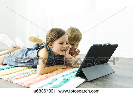 Siblings (2-3, 6-7) lying down on carpet and watching digital tablet View Large Photo Image Stock Image - Siblings (2-3, 6-7) lying down on carpet and watching digital tablet. Fotosearch