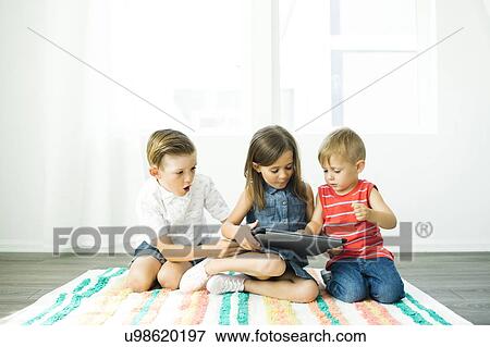 Stock Photo - Siblings (2-3, 6-7) using digital tablet at home. Fotosearch