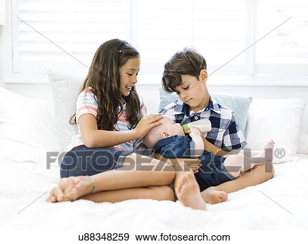 Stock Photo - Siblings ( 6-7, 10-11, 12-17 months ) sitting on sofa. Fotosearch