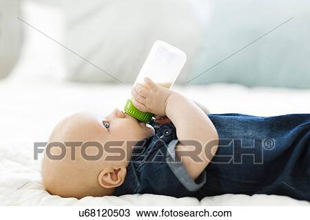 Stock Image - Side view of baby boy ( 12-17 months) drinking milk from bottle. Fotosearch