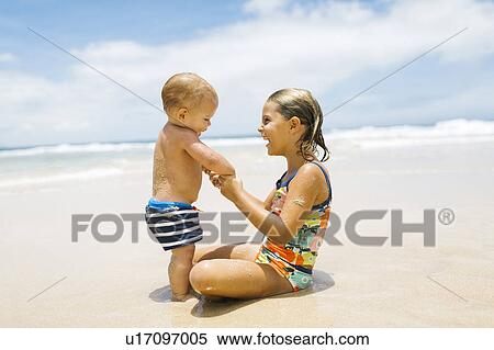 Sister (6-7) holding brother (12-17 months) on beach View Large Photo Image Stock Photography - Sister (6-7) holding brother (12-17 months) on beach. Fotosearch