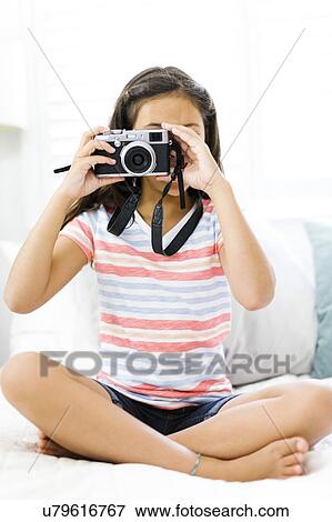 Stock Photo - Sitting girl (10-11) holding camera and taking photo. Fotosearch