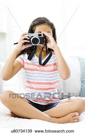 Stock Photo - Sitting girl (10-11) holding camera and taking photo. Fotosearch