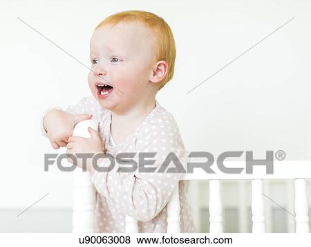 Stock Photo - Small girl ( 12-17 months) with red hair standing in crib. Fotosearch